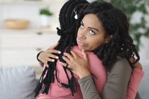 Irritated black lady hugging her girlfriend with annoyed face expression, fake friendship concept. Two african american women embracing, crying lady looking for support, copy space