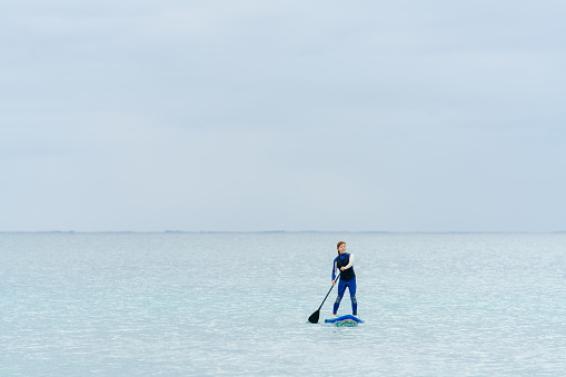 A woman is paddle boarding in a wetsuit in the sea during winter.