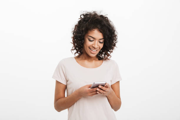 istock Content smiling woman with afro hairstyle typing text message or using internet on smartphone, isolated over white background 1290501170