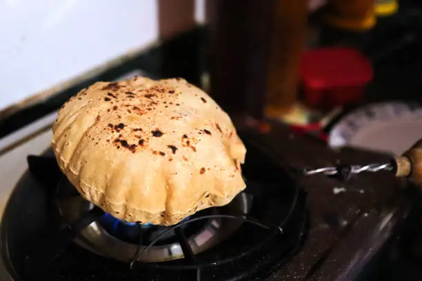 close up shot of cooking a roti or chappati being roasted puffed and swollen on a blue gas flame in the kitchen.