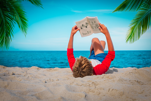 boy reading book at beach vacation, summer reading concept