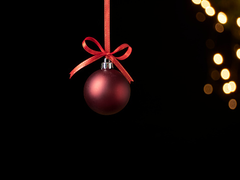 Christmas ball hanging on dark background against blurred festive lights. Space for text