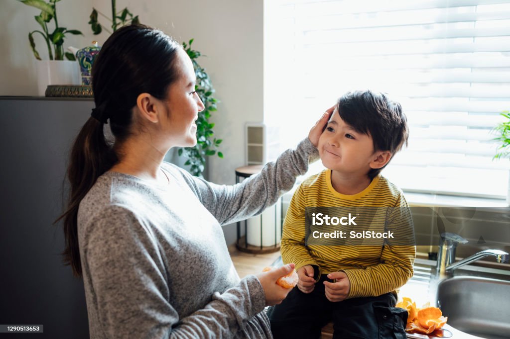 I Love You Mother and son spending time together in the kitchen of their home. The mother is stroking her sons head while he sits on the kitchen counter. She is peeling a tangerine for him.  They are in the Northeast of England. Mother Stock Photo