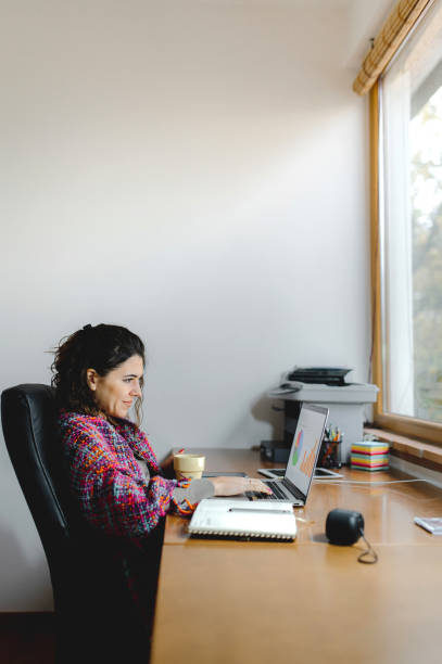 istock Woman holding a cup of hot drink with blanket while working at computer desk. 1290517728