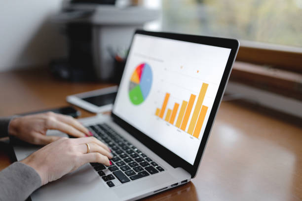 istock Close-up workplace with computer laptop and Histograms representation on pc screen with woman hands typing. 1290518983