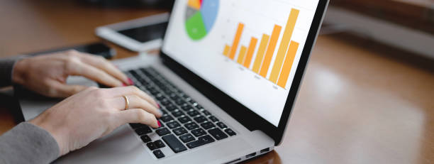 istock Close-up workplace with computer laptop and Histograms representation on pc desktop with woman hands typing. 1290521100