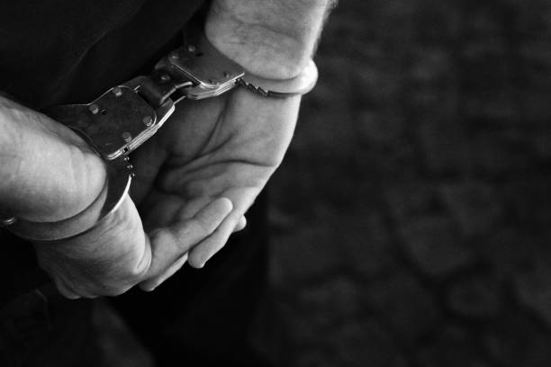 Man's hands handcuffed behind his back as he stands waiting for the next step in the criminal justice system Man with his hands handcuffed behind his back. criminal justice stock pictures, royalty-free photos & images