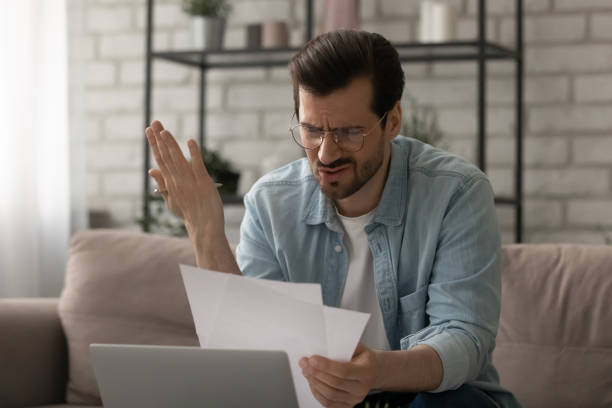 istock Frustrated young man in glasses looking at paper, feeling stressed. 1290529090