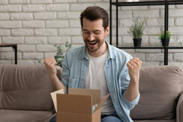 istock Happy young man in eyeglasses opening small cardboard parcel. 1290529114