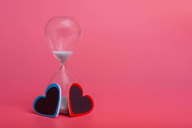 Two hearts and an hourglass on a pink background. the concept of love and happiness.