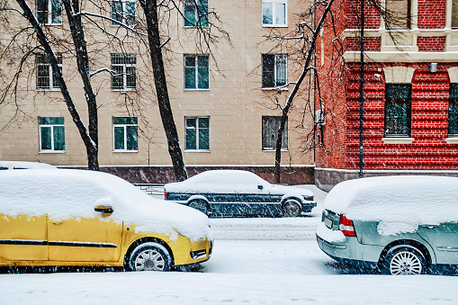 Red and blue cars covered by snow parked on Moscow street after snowstorm