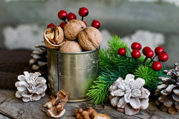 Walnuts in a tin, whole and split, next to the filling and shell. Presented in a New Year's composition with cones, red berries and a sprig of a Christmas tree. Home storage of winter preparations