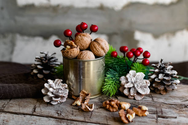 Walnuts in a tin, whole and split, next to the filling and shell. Presented in a New Year's composition with cones, red berries and a sprig of a Christmas tree stock photo