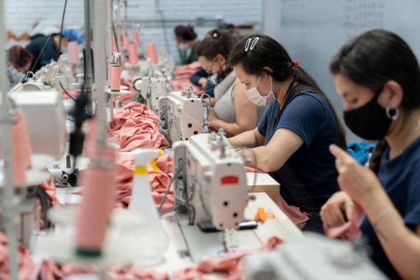 donne che lavorano in una fabbrica tessile indossando una maschera facciale mentre cucino vestiti - manual worker sewing women tailor foto e immagini stock