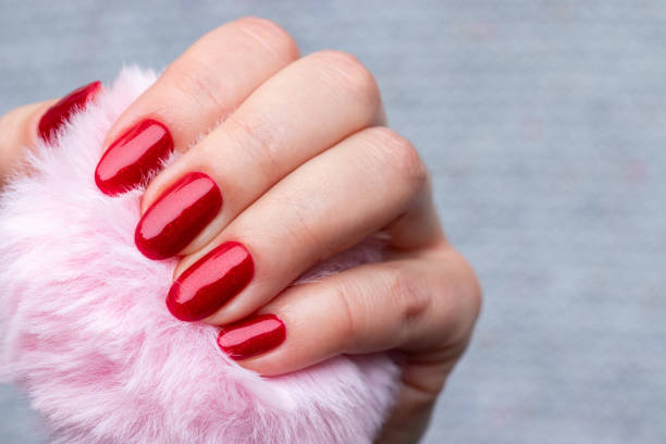 istock Female hand with pink fluffy ball with beautiful manicure - red glittered nails. Selective focus. Closeup view 1290534362