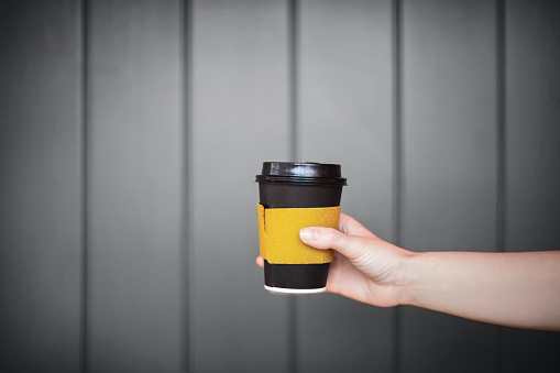 Cup of coffee to go in a female hand on a background of gray wall