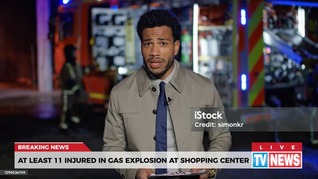 News reporter reporting on gas explosion Male news reporter reporting on gas explosion at shopping centre during night. Newscaster Stock Photo