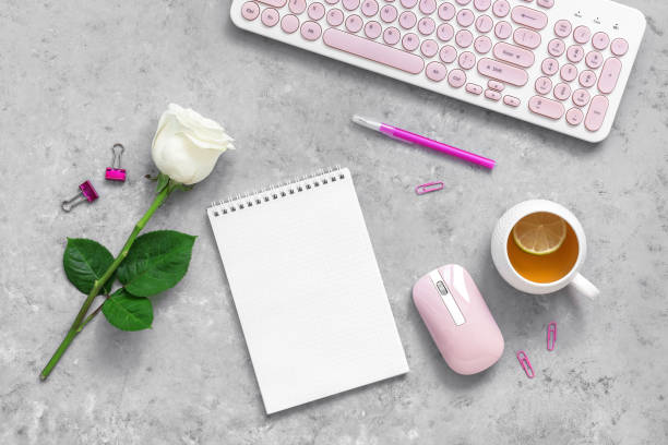 istock Feminine freelance workspace concept. Workplace of a freelancer or office worker. Keyboard, blank notepad, mouse, cup of tea and rose flower. Top view, flat lay. Gray concrete grunge background. 1290538381