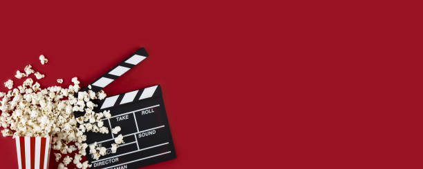 istock Watching movie with popcorn and clapperboard on red background. Long wide banner 1290538885