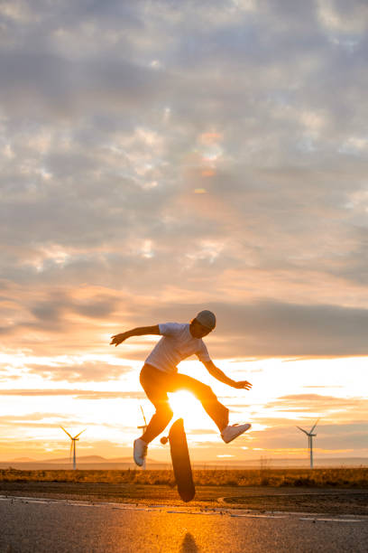 Silhouette Skateboarding In The Sun A young man jumping up and his body silhouetted against the sun setting across the moors and beautiful Scottish Highlands. golden hour photos stock pictures, royalty-free photos & images