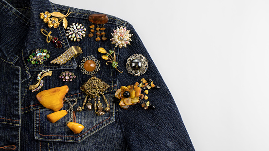 Beautiful  rare vintage brooches with amber, sparkling crystals gemstones and pearls are pinned on the dark blue denim jacket. Isolated object on the white background.