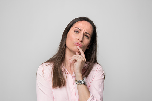 Portrait of thoughtful mid adult woman standing against grey background.
