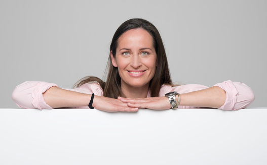 Portrait of smiling mid adult woman leaning on polystyrene while standing against grey background.