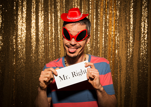 Portrait of smiling mid adult man wearing funny props and showing poster while posing in photo booth.