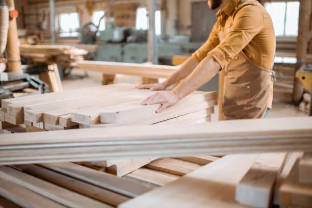 istock Carpenter carrying pine planks in the warehosue 1290549038