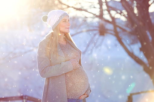 Happy pregnant woman outdoors, nice future mom enjoying beautiful winter snowy day and bright sun light, family love and new life concept