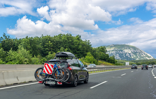Razdrto, Slovenia – July 19, 2020: Black car with roof luggage box and trunk bike rack driving on the highway. Beautiful mountain landscape background