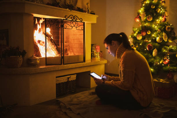 istock Woman relaxing with e-book near fireplace and Christmas tree. 1290553536