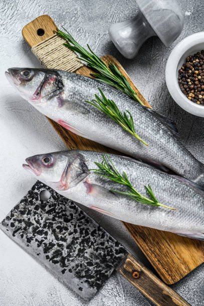 istock Raw seabass fish on a cutting board with spices, herbs. White background. Top view 1290553666