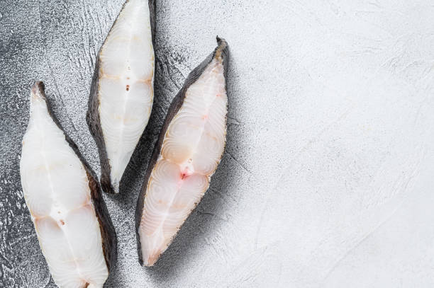 istock Raw fresh steak fish halibut on the stone table. White background. Top view. Copy space 1290554365