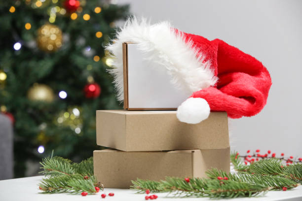 istock Blank cardboard boxes with Santa hat on the table in festive Christmas setting. Simple gift box with copy space. 1290556018