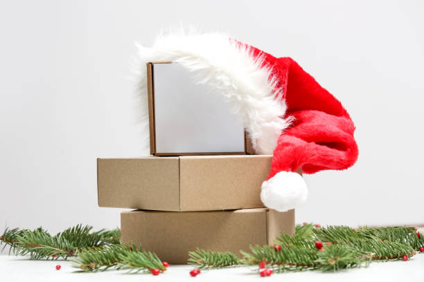 istock Blank cardboard boxes with Santa hat on the table in festive Christmas setting. Simple gift box with copy space. 1290556342