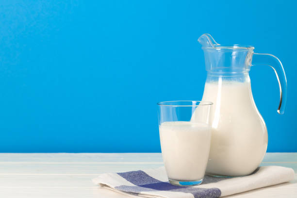 istock Glass and pitcher of milk against blue background 1290559622