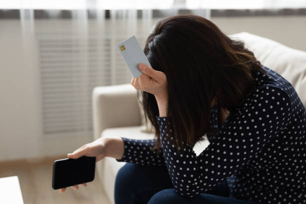 Close up unhappy Asian woman holding plastic card and phone Close up unhappy frustrated Asian woman holding white empty mock up plastic card and phone, touching head, crying, having problem with credit card, loss money, internet fraud and scam concept money cry stock pictures, royalty-free photos & images