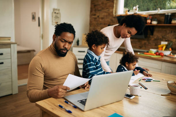 istock Black working father analyzing paperwork while mother is assisting their kids with homework at home. 1290561569