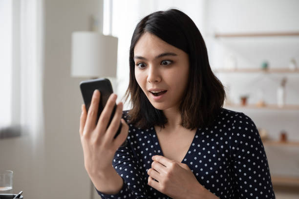 istock Close up amazed Asian woman looking at phone screen 1290561621