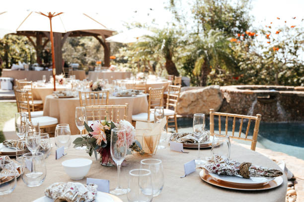 istock Rustic backyard wedding - reception tables with golden plates and chairs, dahlias, peonies and eucalyptus leaves and jute rope napkin rings. 1290561836