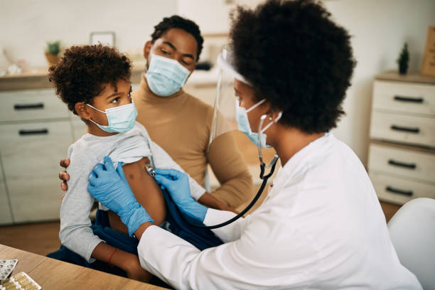 Small black boy having medical exam at doctor's office during coronavirus pandemic. African American boy with face mask being examined by female pediatrician during medical apportionment at doctor's office. lung photos stock pictures, royalty-free photos & images