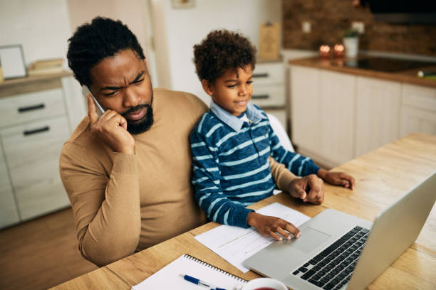 istock Black working father talking on the phone while son is sitting on his lap at home. 1290563309