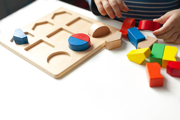 Educational toys, Cognitive skills, Montessori activity. Closeup: Hands of a little Montessori kid learning about color, shape, sorting, arranging by engaged colorful wooden sensorial blocks. Educational toys, Cognitive skills, Montessori activity. Closeup: Hands of a little Montessori kid learning about color, shape, sorting, arranging by engaged colorful wooden sensorial blocks. montessori education stock pictures, royalty-free photos & images