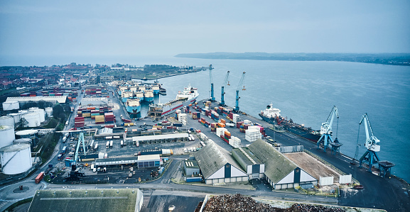 Drone point of view in Danish harbor. Cranes and heavy machinery along with fuel tanks and warehouses at the waterfront