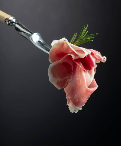 Sliced prosciutto with rosemary on a fork.