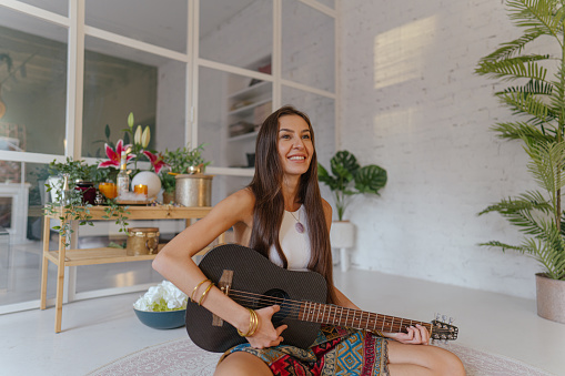 Photo of a young woman, a new age movement follower, playing guitar in her home as a form of music therapy