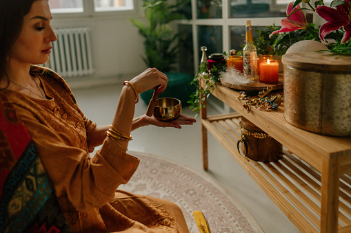 Photo of a young woman, practicing meditation and reading prayers while using Tibetan singing bowl.