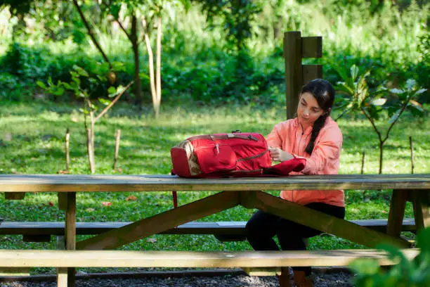 Young female explorer hiker enjoying nature forest. Girl having rest and looking into her equipment sitting a the table