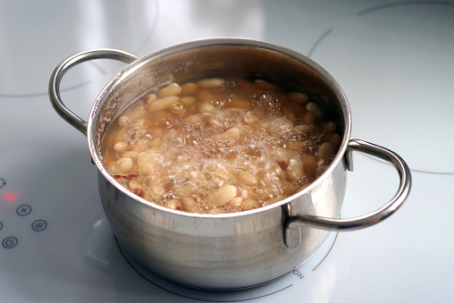 Plain dry beans are cooked in a saucepan on an induction hob.